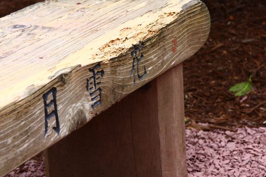 Wooden bench in a garden with Japanese inscriptions.