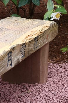 Wooden bench in a garden with Japanese inscriptions.