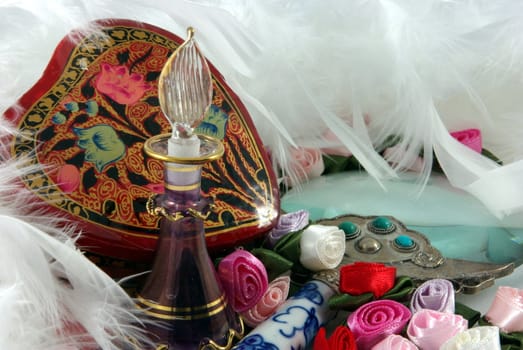 A small perfume bottle nestled among flowers and white feathers