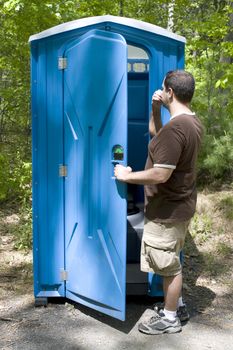 A young man investigating a blue porta potty located on the hiking trail.  Desperate times call for desperate measures.