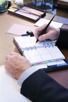 Business mans hands writing in day planner at desk
