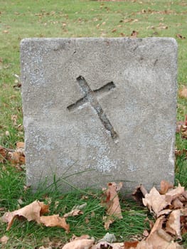 Small graveyard headstone with cross. Stone has moss and lichen on it. 