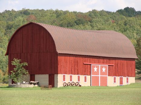 Long red barn with stone foundation. Barn has white stars on the doors, Early fall color in the hillside background.