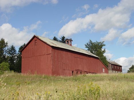 Long red barn in summer field against blue sky and clouds.