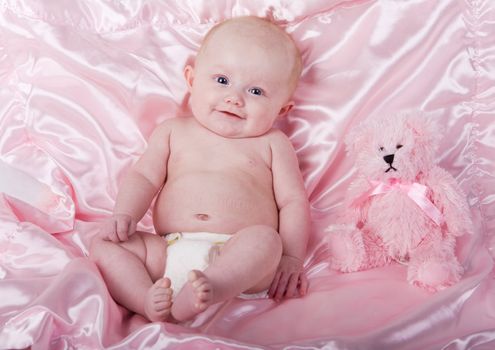 A baby girl on a pink blanket with a teddy bear