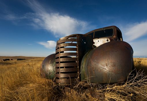 vintage truck abandoned and rusting away in the prairies, ghost town in the background