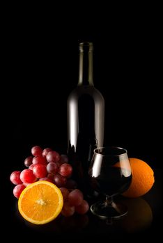 Fruits and bottle of wine on black background with reflection