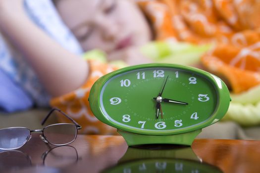 Green clock and glasses with a female sleeping in the background(shallow dof)