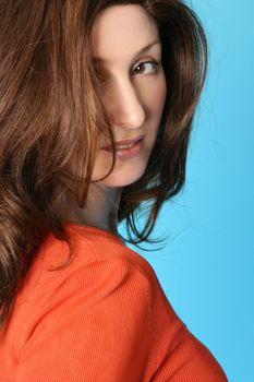 Female with brown hair tinted auburn and strawberry blonde higllights and wearing natural makeup, looking over her shoulder - aqua background