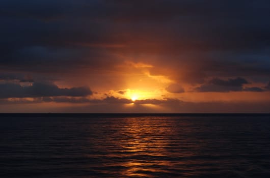 Rays of sunlight emit from a cloud as the sun sets over the ocean.