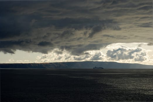 Storm clouds gather over a ship at sea.