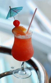 A tropical fruit drink with cherry, orange and a blue umbrella.