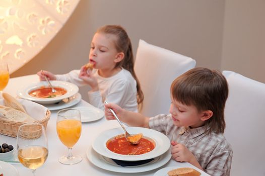 Sister and brother enjoying meal sitting at restaurant table. Boy in focus, girl out of focus.