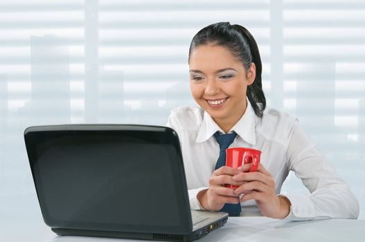 Young woman looks at her laptop computer and drinks her coffee