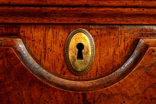 Wooden door of an ancient desk with a decorative metal plate for a key.