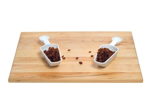 Two scoops of raisins shot on a wooden cutting board, all isolated against a white background
