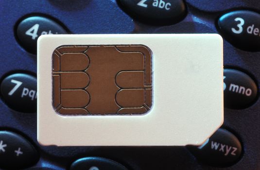 A mobile phone sim card on top of a phone keypad.