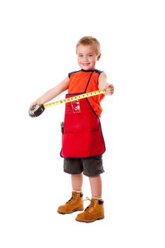 A Caucasian male young child dressed in an orange apron and construction boots holding yellow measuring tape, isolated.