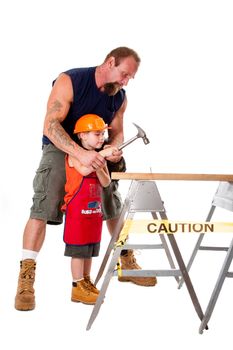 Caucasian father teaching his cute son how to hild a hammer and hit a nail into a wooden plank, isolated.