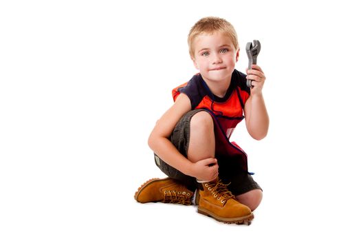 Cute young boy holding toy wrench while sitting, isolated.