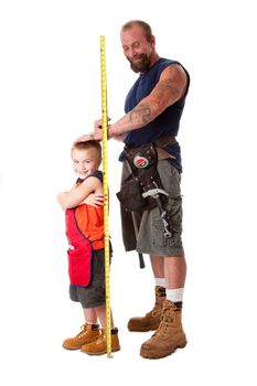 Father wearing tool belt with toy hammer and measuring tape, measures height of cute son dressed in orange apron, isolated.