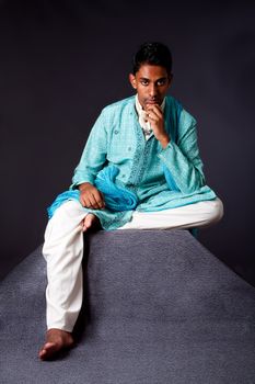 Beautiful authentic Indian hindu man in typical ethnic groom attire sitting and thinking on top of pyramid rock. Bangali male wearing a light blue agua decorated Dhoti with shawl.