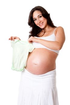Beautiful happy smiling pregnant woman dressed in white holding a green striped baby bodysuit next to her bare belly, isolated