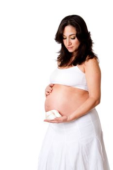 Beautiful happy pregnant woman dressed in white holding a pair of yellow baby shoes next to her bare belly, isolated