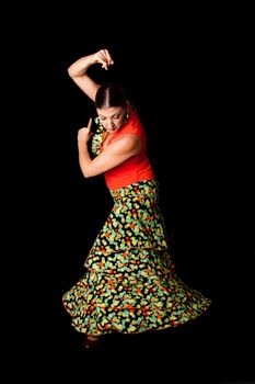 Beautiful Spanish Caucasian Flamenco and Paso Doble dancer wearing a colorful skirt with polka dots and orange shirt doing a line pose, isolated on black.