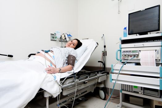 Pregnant Caucasian Hispanic Latina woman laying in a hospital gurney bed in the triage unit doing a medical non stress test (NST) while being hooked up to a computer for monitoring.