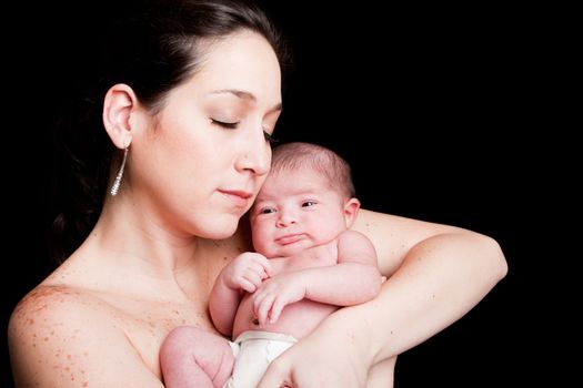 Beautiful Caucasian Hispanic mother with eyes closed holding her newborn baby with open eyes and diaper in her arms, isolated.