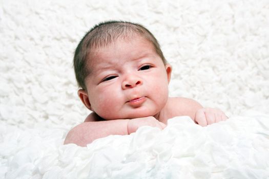 Cute Caucasian Hispanic infant baby face with funny expression on soft white cotton cloud.