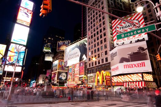 Night scene of Broadway at Times Square in Manhattan (New York City) with all the lit up billboards and advertisements, and many tourists people walking by.