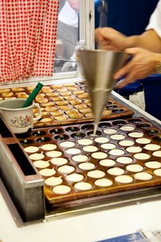 Delicious authentic Dutch food from The Netherlands called poffertjes, which are mini pancakes, being prepared on a typical hot plate while cook is pouring new batter into hot plate.