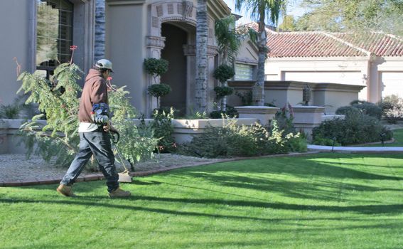 man trimming edges of grass at upscale home