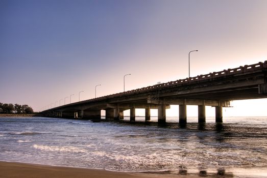 Landscape of sunset with bridge over ocean.