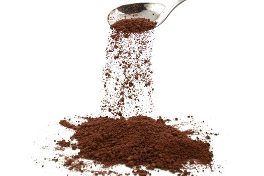 cocoa powder trickling of a silver spoon with white background