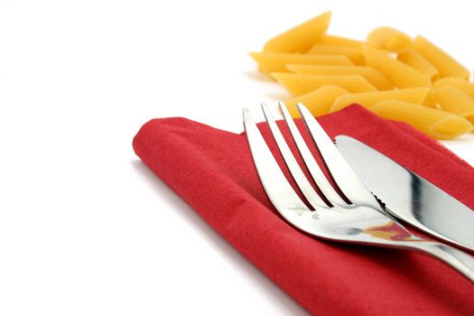 fork and knife on red napkin with pasta in the background