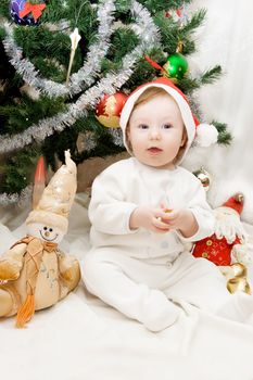 Baby in santa hat sitting under Christmas tree