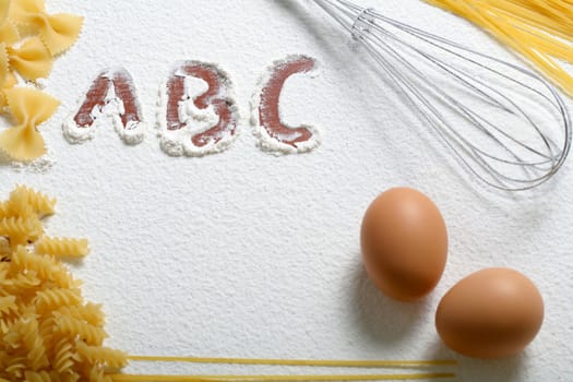 Uncooked macaroni, whisk and eggs on wheat flour, background