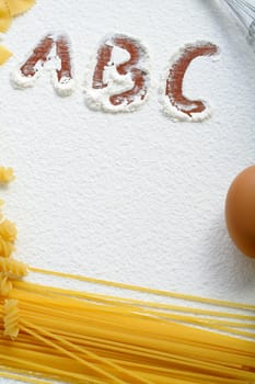 Uncooked macaroni and egg on wheat flour, background