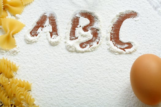 Uncooked macaroni and egg on wheat flour, background