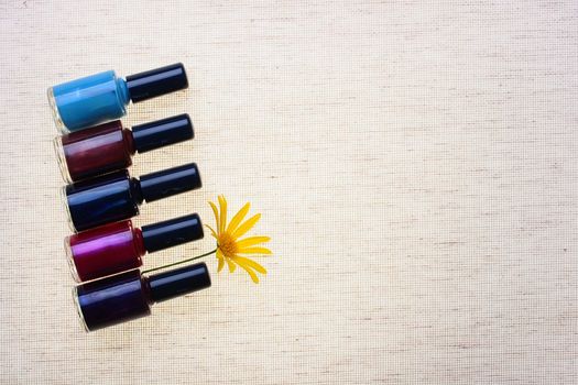 Set of nail polish against from a grey fabric with a yellow flower.