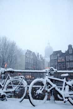 A bicycle stands under heavy snowstorm on background with buildings in Amsterdam