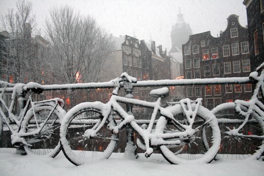 A bicycle stands under heavy snowstorm on background with buildings in Amsterdam