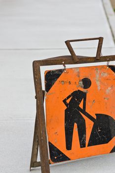Closeup of an orange construction sign denoting men at work, on a newly made sidewalk.