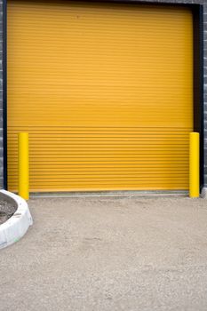 A colorful industrial garage door, with yellow barriers on either side.  This door is actually on the side of a hockey rink, for Zamboni's to exit the rink and dump the snow that they scraped from the ice.