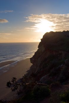 Silhouette of the cliffs near Lagos, Portugal, as the sun sets, shot into the sun, with the deserted beach below.