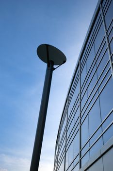 The corner of a curvy, glass office building, against a blue sky, with a lamp post in the middle of the image.  University of Guelph, Guelph, Ontario, Canada
