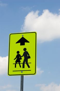 A street sign indicating that people are crossing ahead, isolated on a blue sky with some sporadic clouds.